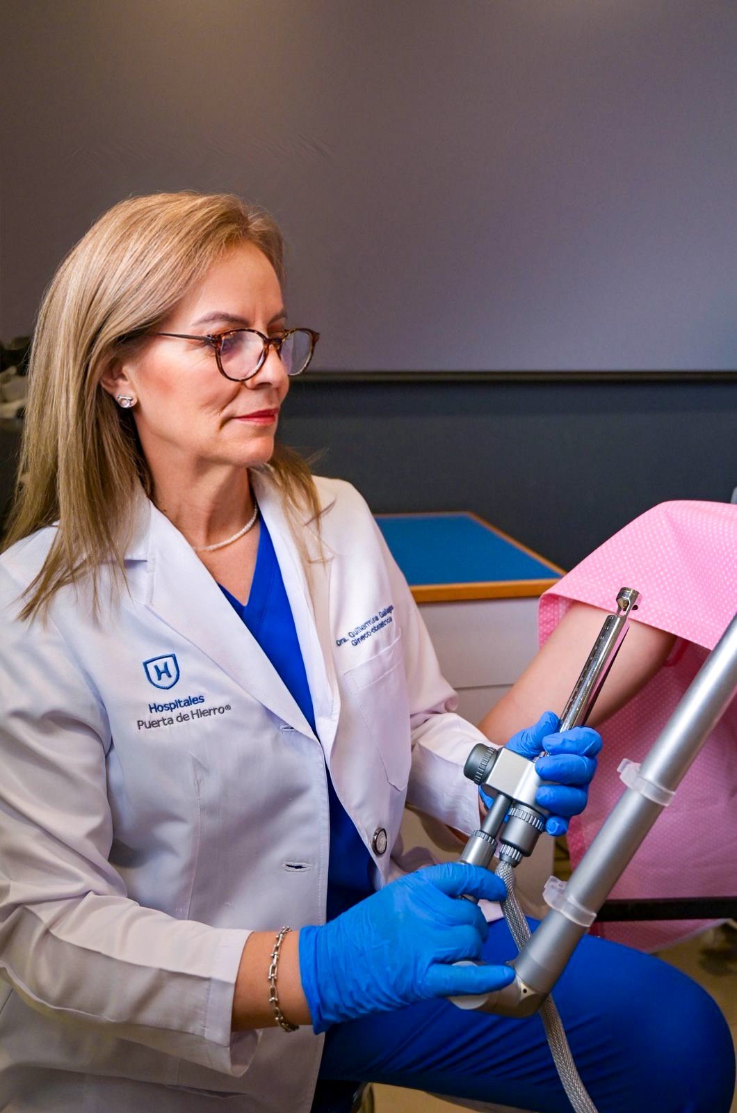 Female healthcare professional in white lab coat and blue gloves holding medical equipment while looking at a pink object